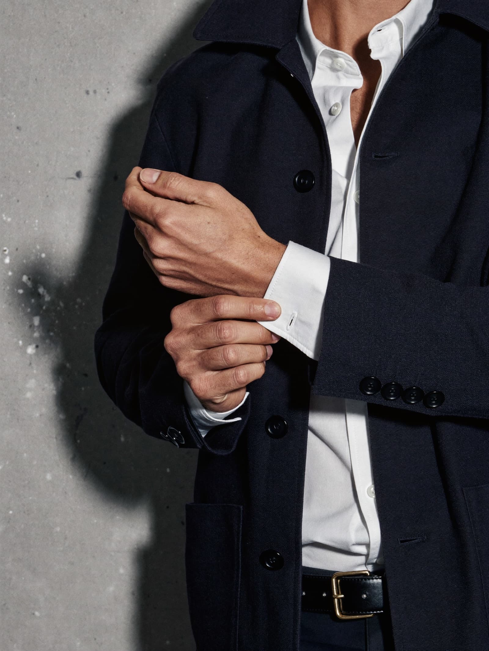 Main ajustant le poignet d'une chemise blanche sous une veste de laine bleu nuit